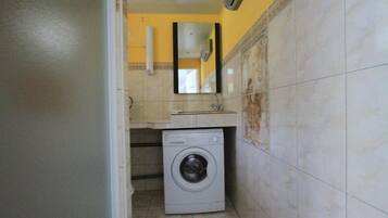 A compact laundry room with a washing machine, a sink, and a mirror.