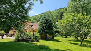 A yellow building with a tiled roof, surrounded by lush greenery and trees. - DOMAINE DES GRAVIERS (Plainfaing)