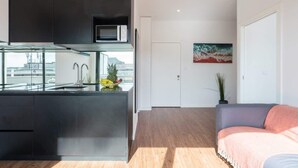 A modern kitchen with dark cabinets, a microwave, and a fruit bowl. There is a wooden floor, a gray sofa, and a painting on the wall. - Bright Flat w/ Balcony |  Ace Location by HostWise (Porto)