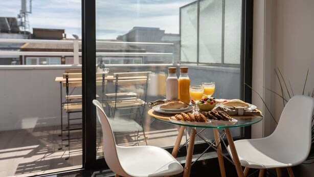 A modern dining area with a glass table and white chairs, overlooking a cityscape. - Bright Flat w/ Balcony |  Ace Location by HostWise (Porto)