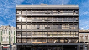 A modern multi-story building with a glass facade, featuring storefronts on the ground level. - Bright Flat w/ Balcony |  Ace Location by HostWise (Porto)