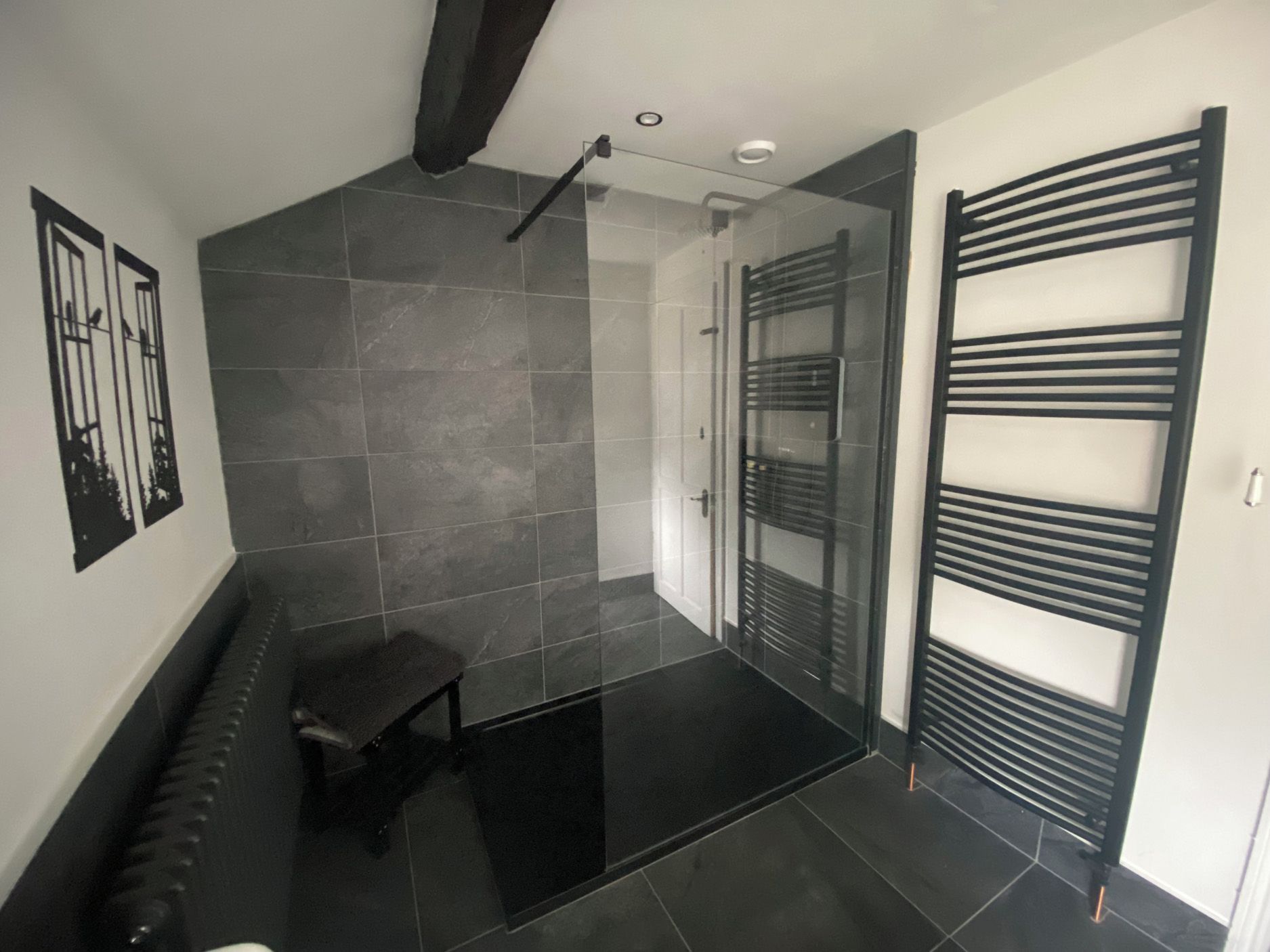 A modern bathroom with a glass shower enclosure, a bench, and a towel rack.