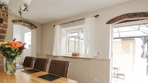Un comedor con una mesa de madera, sillas de cuero marrón, un florero con flores y una ventana con cortinas blancas.