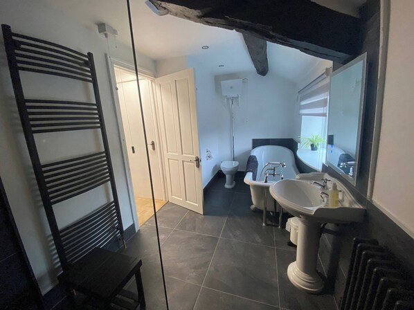 A bathroom with a bathtub, a sink, and a toilet. There is a door leading to another room. - The Hollies (Carlisle)