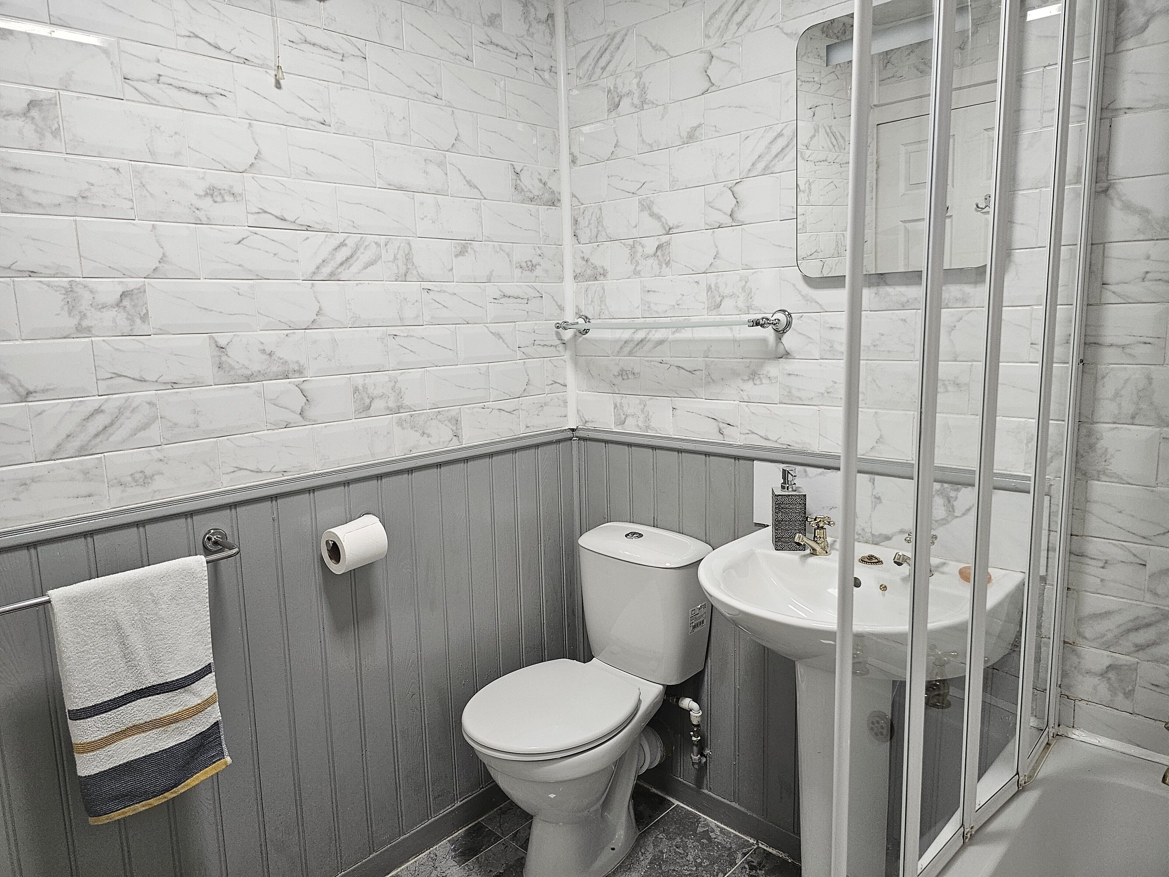 A bathroom with marble tiles, a toilet, a sink, and a glass shower enclosure.