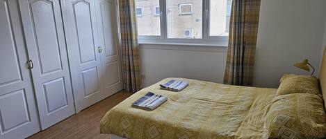 A bedroom with a bed, a window, curtains, and a door.