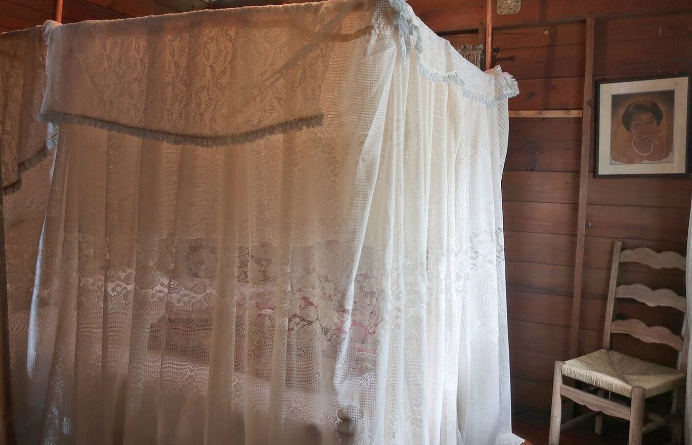 A room with a wooden wall, a white lace curtain, and a wooden chair.