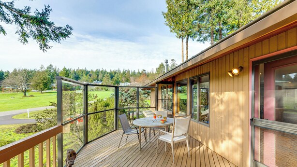A wooden deck with a table and chairs, overlooking a green landscape. - Serene La Conner Retreat w/ Fireplace & Deck! (La Conner)