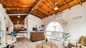 Amplio espacio interior con vigas de madera, mostrador de recepción, zonas de estar y vistas a través de un ventanal arqueado.