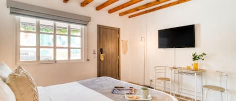 Un dormitorio con cama, escritorio, silla, televisor y ventana con persianas.