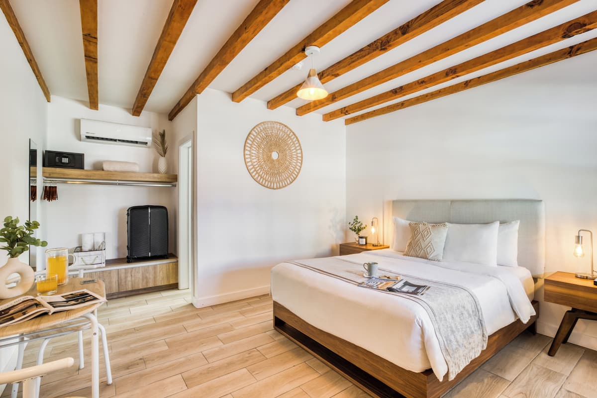 A modern bedroom with a wooden ceiling, a large bed, bedside tables, a desk with a chair, and a wall-mounted air conditioner.