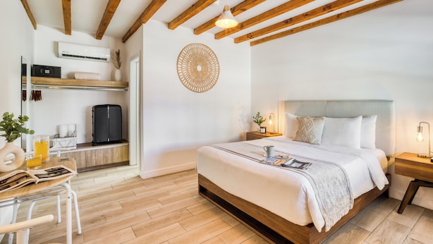Un dormitorio moderno con techo de madera, una cama grande, mesitas de noche, un escritorio con silla y aire acondicionado instalado en la pared.