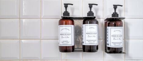 Three bottles of 'Ámbar de Agave' shampoo and conditioner on a tiled wall.