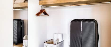 Una habitación con un estante de madera, una maleta negra, un caja de almacenamiento blanca y un perchero.