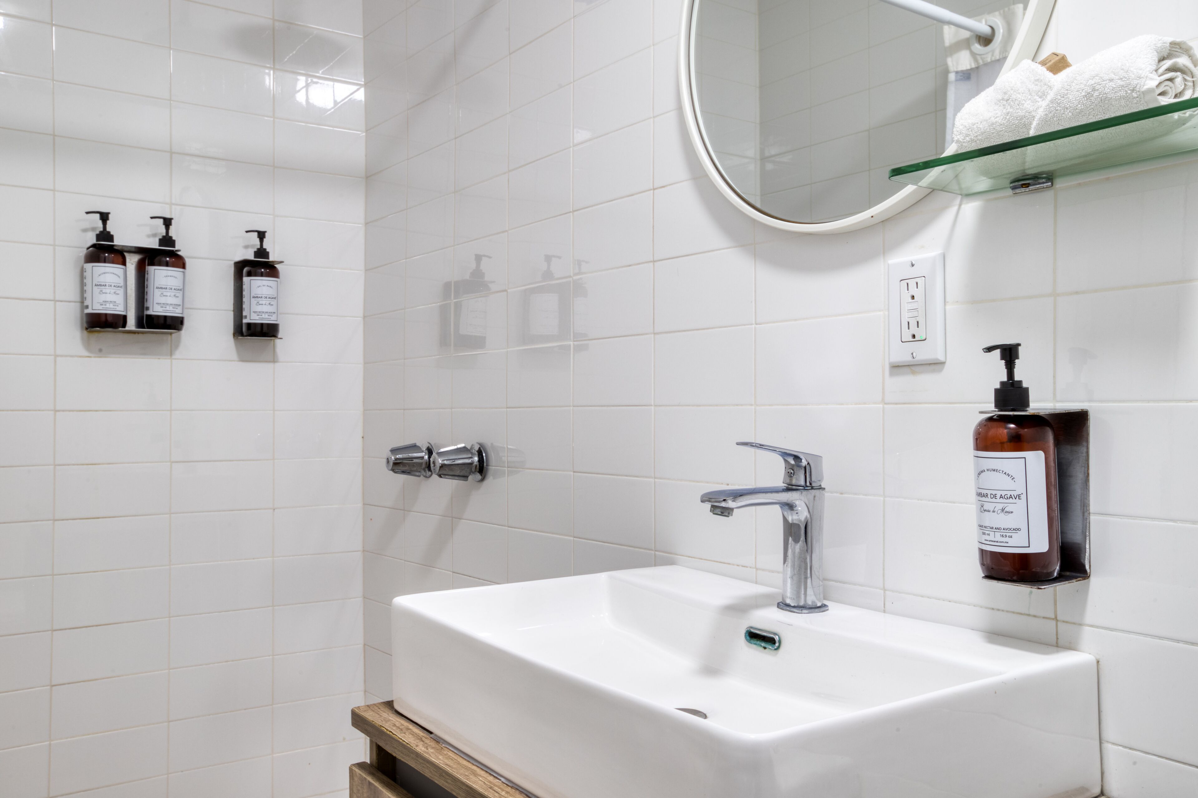 A bathroom with a white sink, two faucets, a mirror, and a glass shelf with a towel.