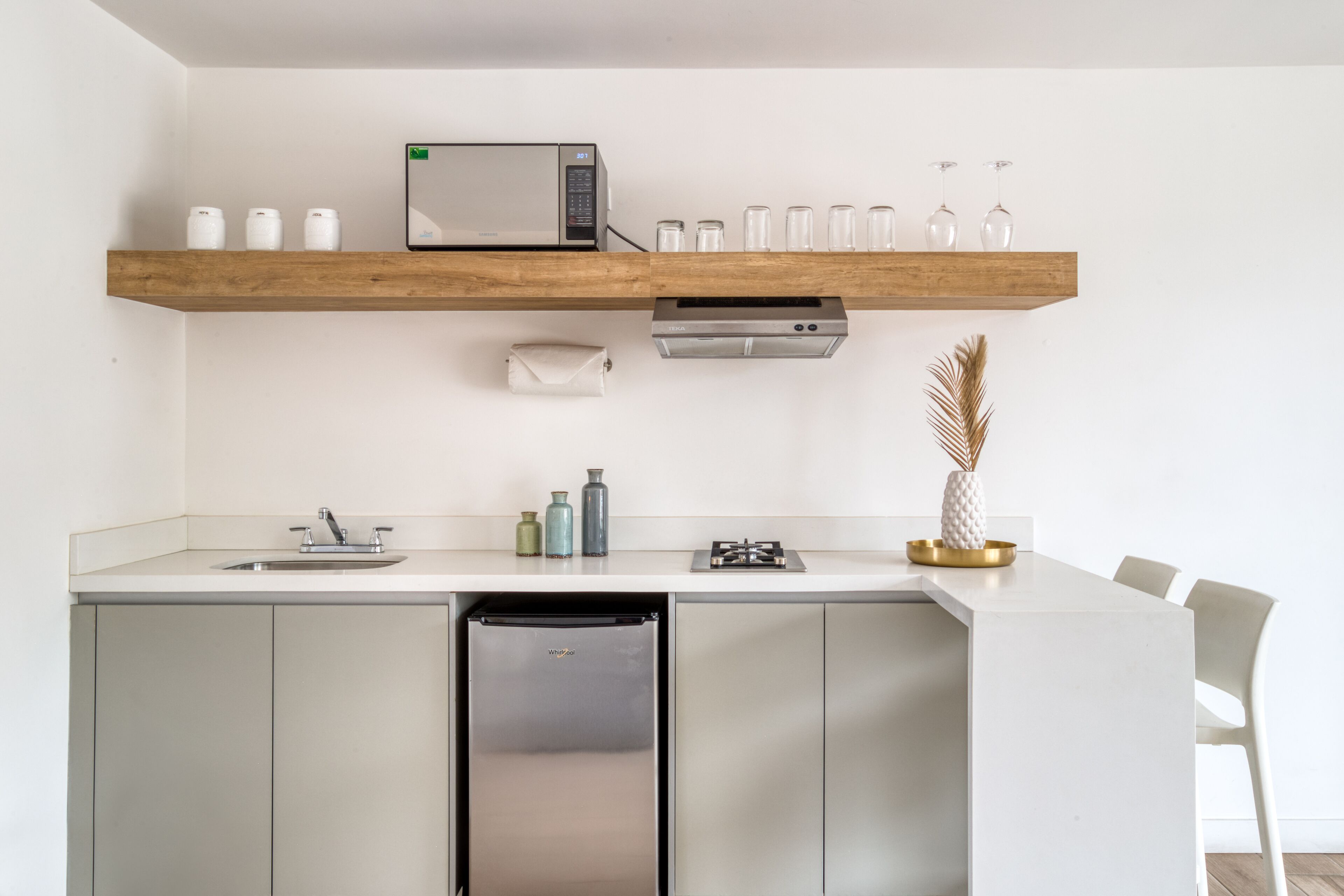 Een moderne keuken met een inbouwmagnetron, broodrooster en gootsteen. Boven het aanrecht staan planken met servies en een decoratieve vaas.