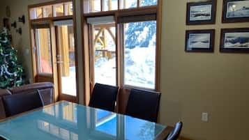 Un coin repas comprenant une table à plateau en verre et quatre chaises, de grandes fenêtres à cadre en bois et un cadre photo fixé au mur.