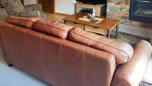 A living room with a brown leather sofa, a wooden coffee table, a stone fireplace, and a television. - Red Rob #6 - 2 bedroom Sleeps 6 (Rossland)