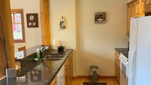 A compact kitchen with wooden cabinets, a granite countertop, a built-in oven, and a small trash bin. - Red Rob #6 - 2 bedroom Sleeps 6 (Rossland)