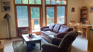 A spacious living room with a leather sofa, a coffee table, and a dining area with wooden chairs and a bookshelf. - Red Rob #6 - 2 bedroom Sleeps 6 (Rossland)