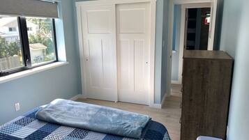 Ein Schlafzimmer mit einem Bett, einem Kleiderschrank, einem Fenster und einer Tür zu einem anderen Raum.