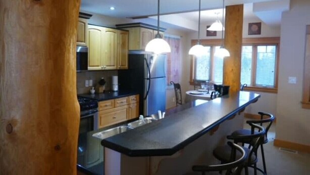 A kitchen with wooden cabinets, a black countertop, and pendant lights. - Redstone Chalets C Red Mountain (Rossland)