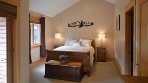 A bedroom with a large bed, two bedside tables with lamps, a wooden bench, and a wall-mounted decoration. - Redstone Chalets C Red Mountain (Rossland)