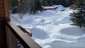 A snowy landscape with a wooden balcony overlooking a snow-covered area and a mountain in the distance. - Redstone Chalets C Red Mountain (Rossland)