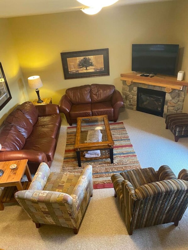 Una sala de estar con un sofá de cuero marrón, un sillón estampado, una mesa de centro de madera, un televisor y una chimenea de piedra.