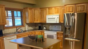 A kitchen with wooden cabinets, a stainless steel refrigerator, a microwave, and a dishwasher. - Copper Chalet 6 - sleeps 10 (Rossland)