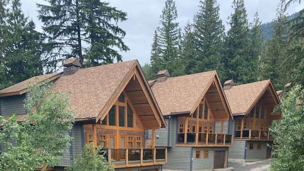 A wooden deck with a view of a row of cabins with sloped roofs and wooden balconies. - Copper Chalet 6 - sleeps 10 (Rossland)