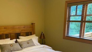 A single bed with a wooden frame, white bedding, and a nightstand with a lamp. - Copper Chalet 6 - sleeps 10 (Rossland)
