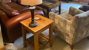 A living room with a leather sofa, a patterned armchair, a small table with a lamp, a fireplace, and a television on a stand. - Copper Chalet 6 - sleeps 10 (Rossland)
