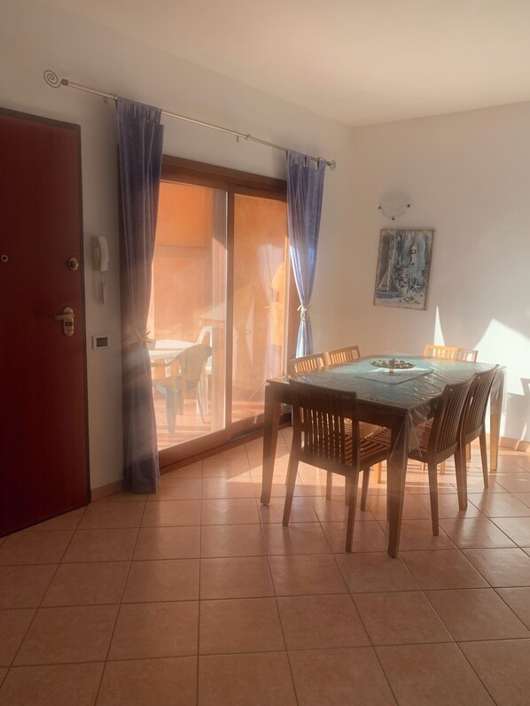 A dining area with a table and chairs, a sliding glass door, and a red door.