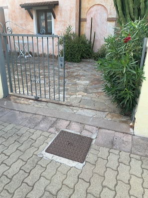 A gated entrance with a metal gate, a stone-paved pathway, and a small metal door.