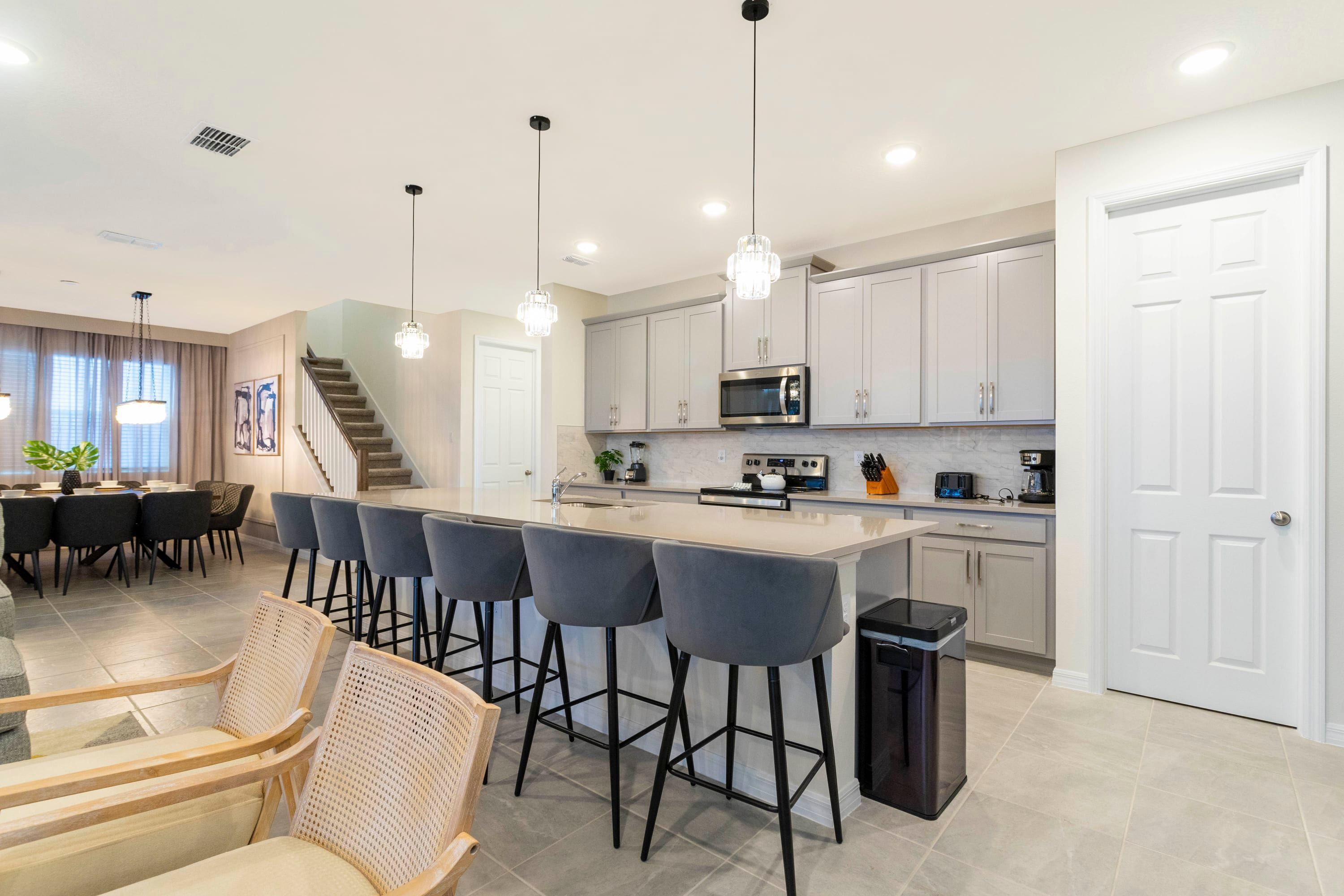 A modern kitchen with a central island, bar stools, and a dining area with a staircase.