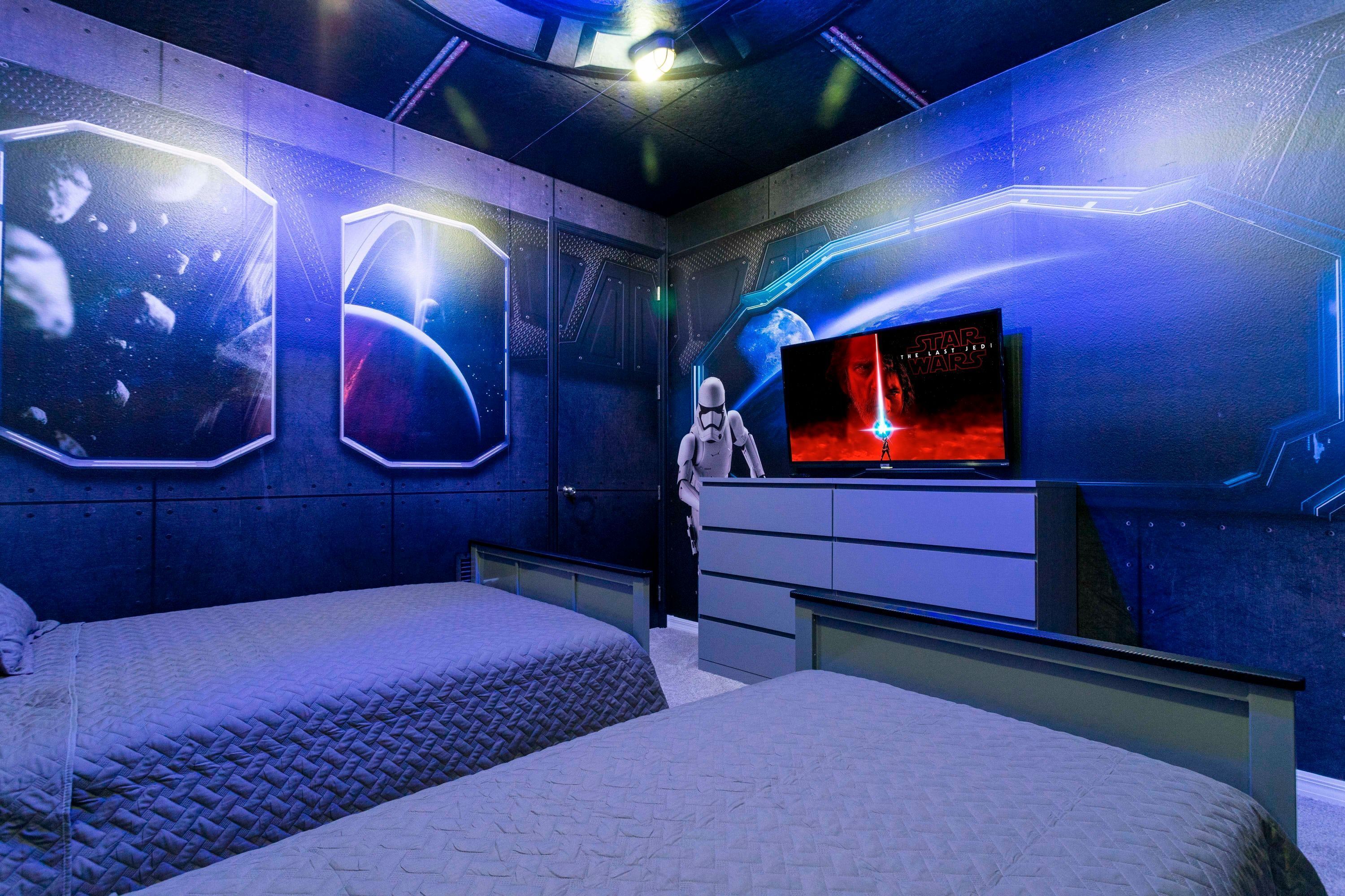 A room with two beds, a Star Wars-themed wall, and a television displaying a Star Wars movie.
