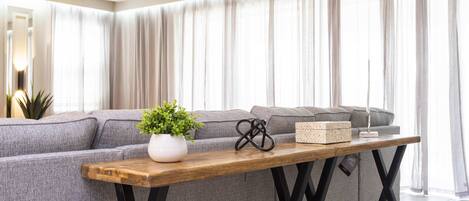 Een moderne woonkamer met een grijze modulaire bank, een houten salontafel en een kroonluchter.