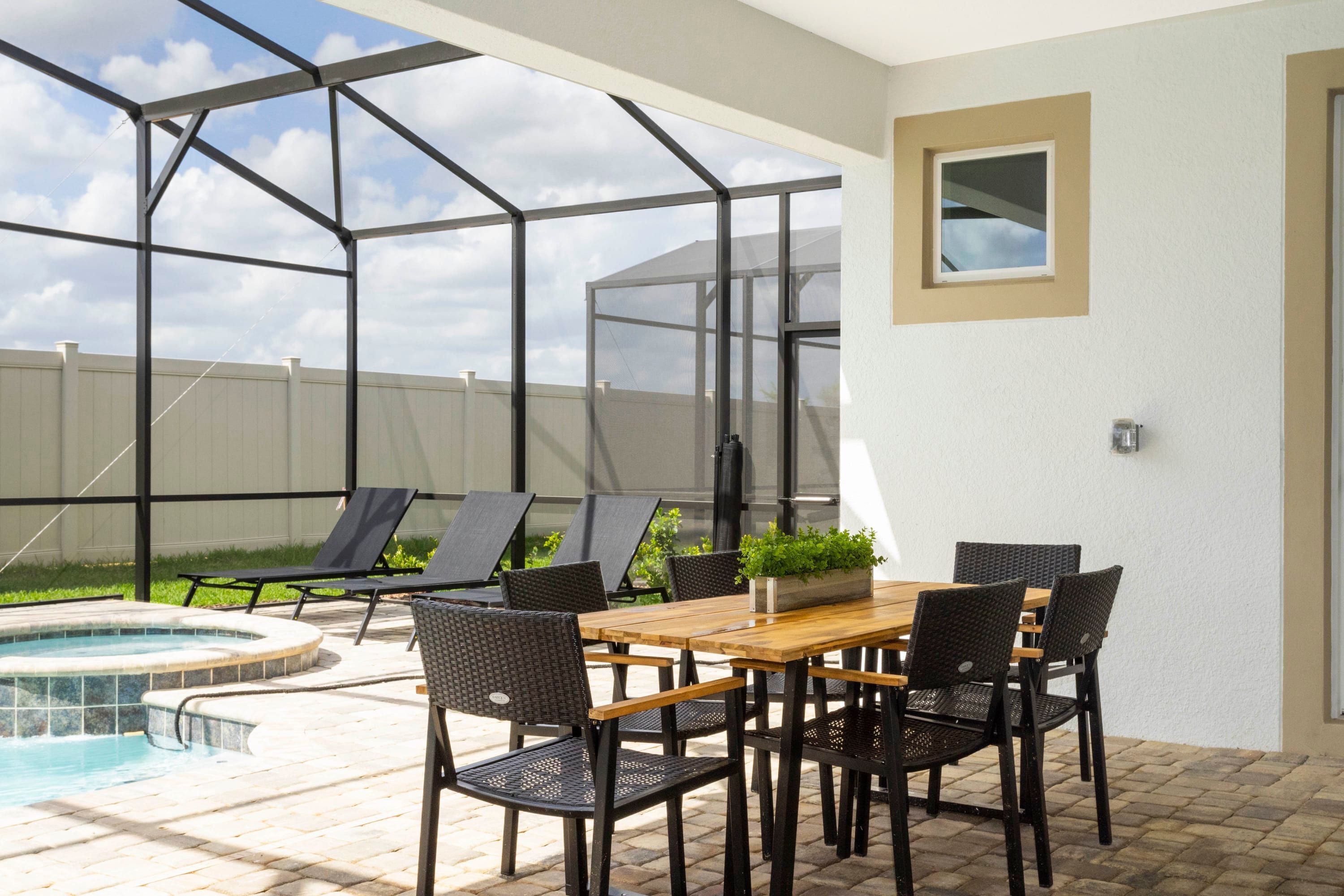 Un espace patio avec une piscine, une table en bois et des chaises, et une vue sur le ciel à travers une structure vitrée.