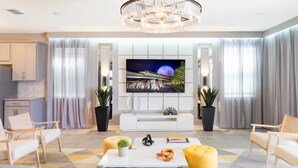 A modern living room with a large flat-screen TV, a chandelier, and a sofa. - Wonderful 9BD 6BA Mariogamer Solararesort Sleep 22 (Kissimmee)