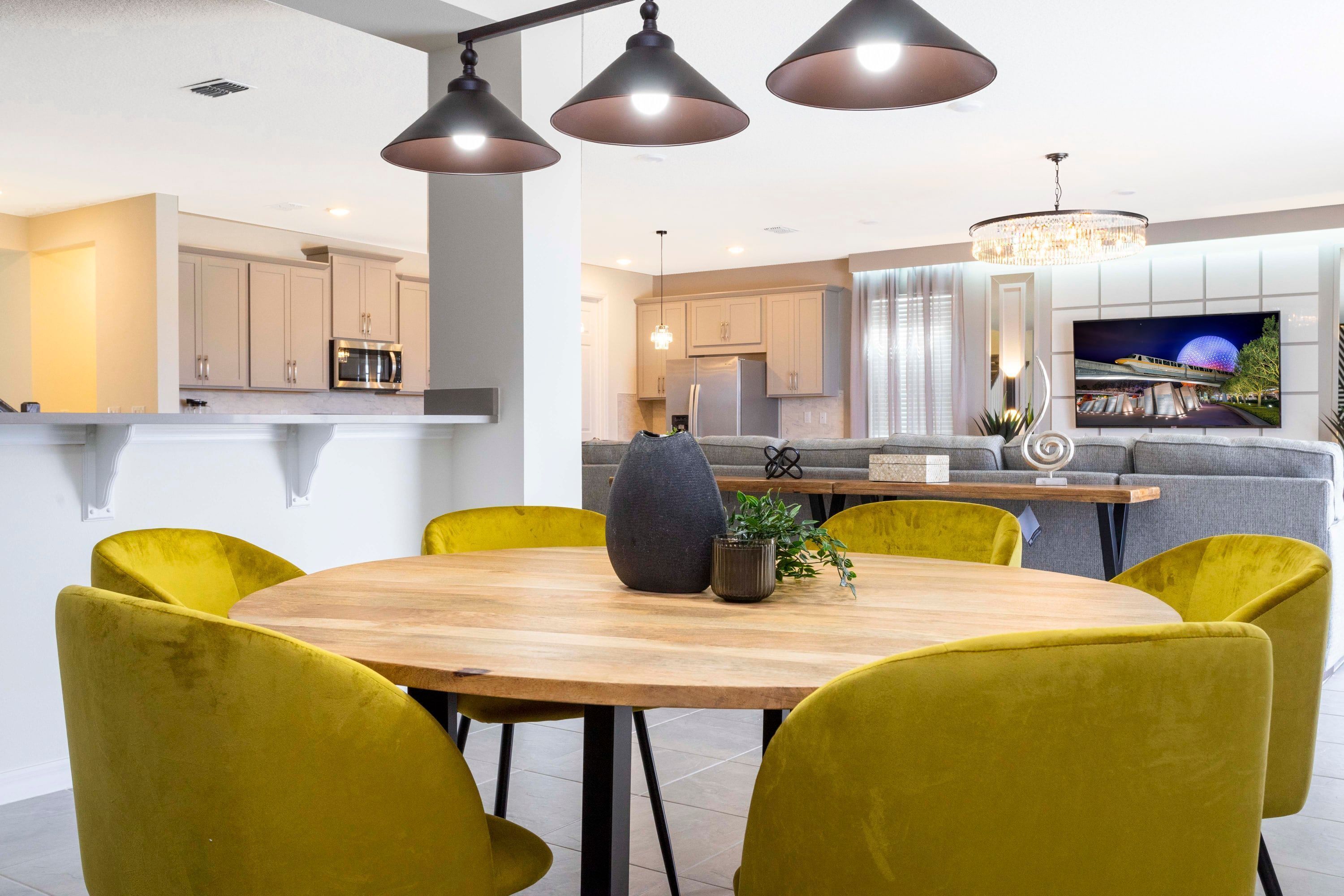 A modern kitchen with a dining area featuring a round wooden table and yellow chairs.