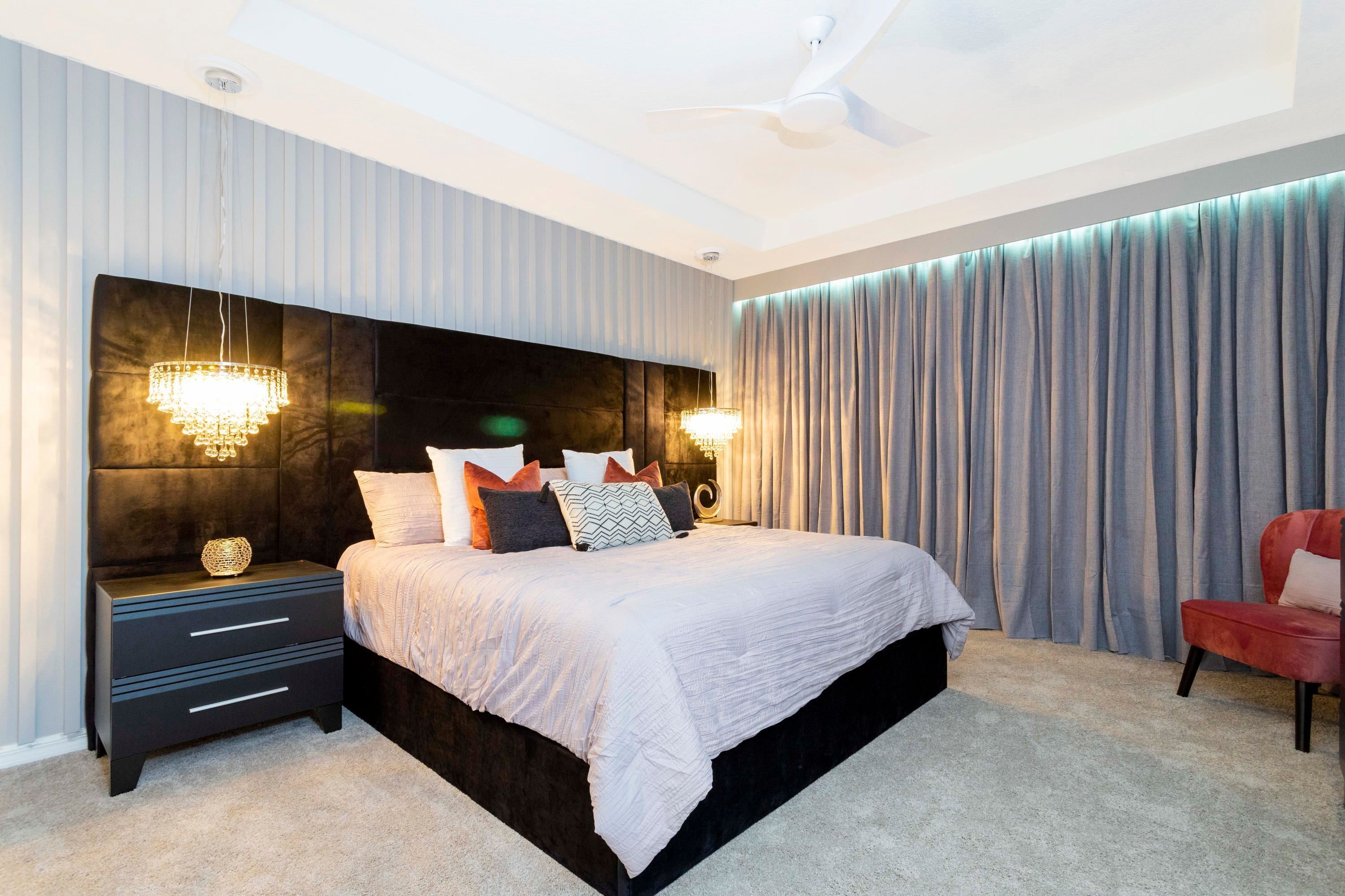 A modern bedroom with a large bed, two bedside tables, a ceiling fan, and a view of the outdoors through curtains.