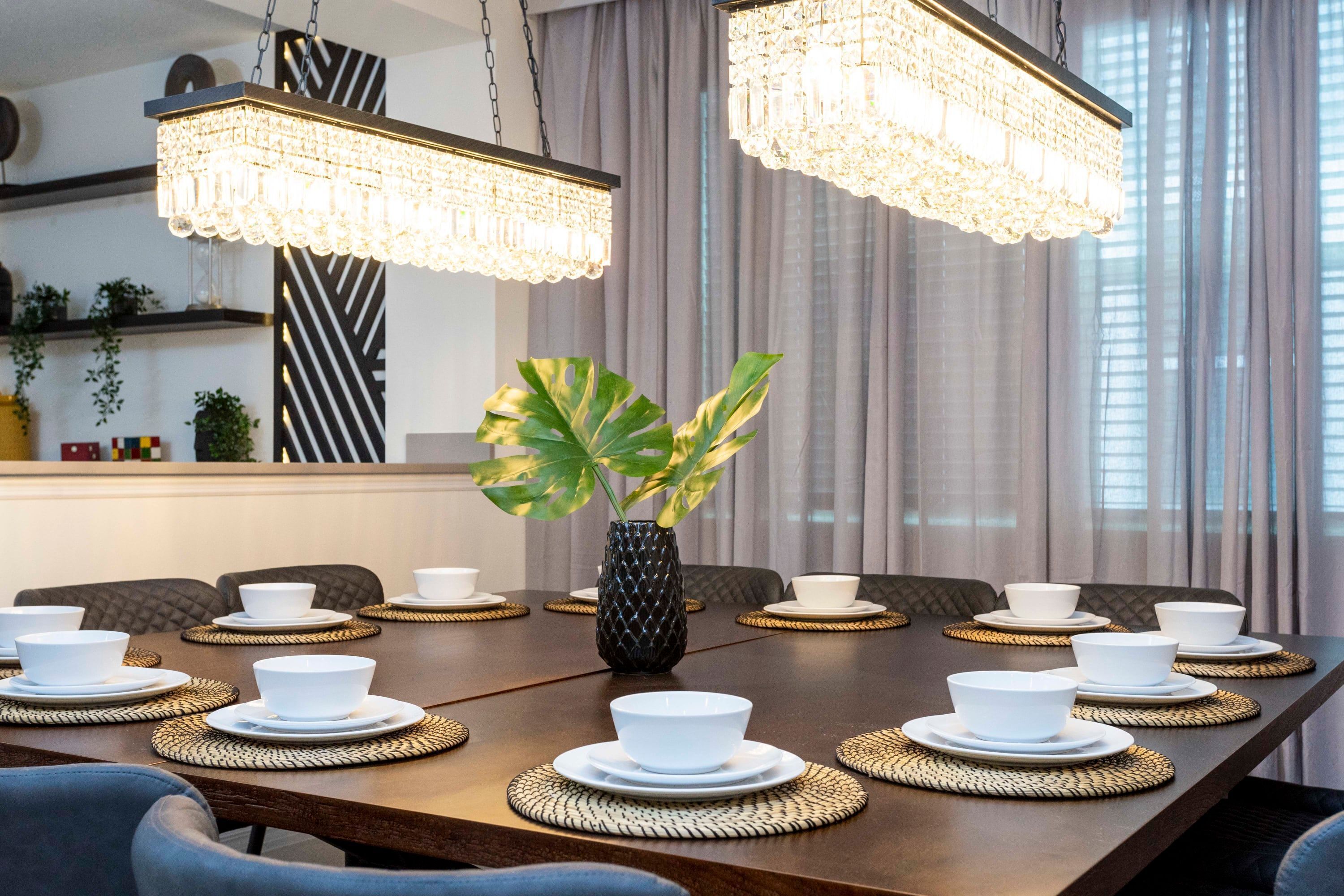 A dining table set with white bowls and plates, surrounded by woven placemats, with a black vase in the center.