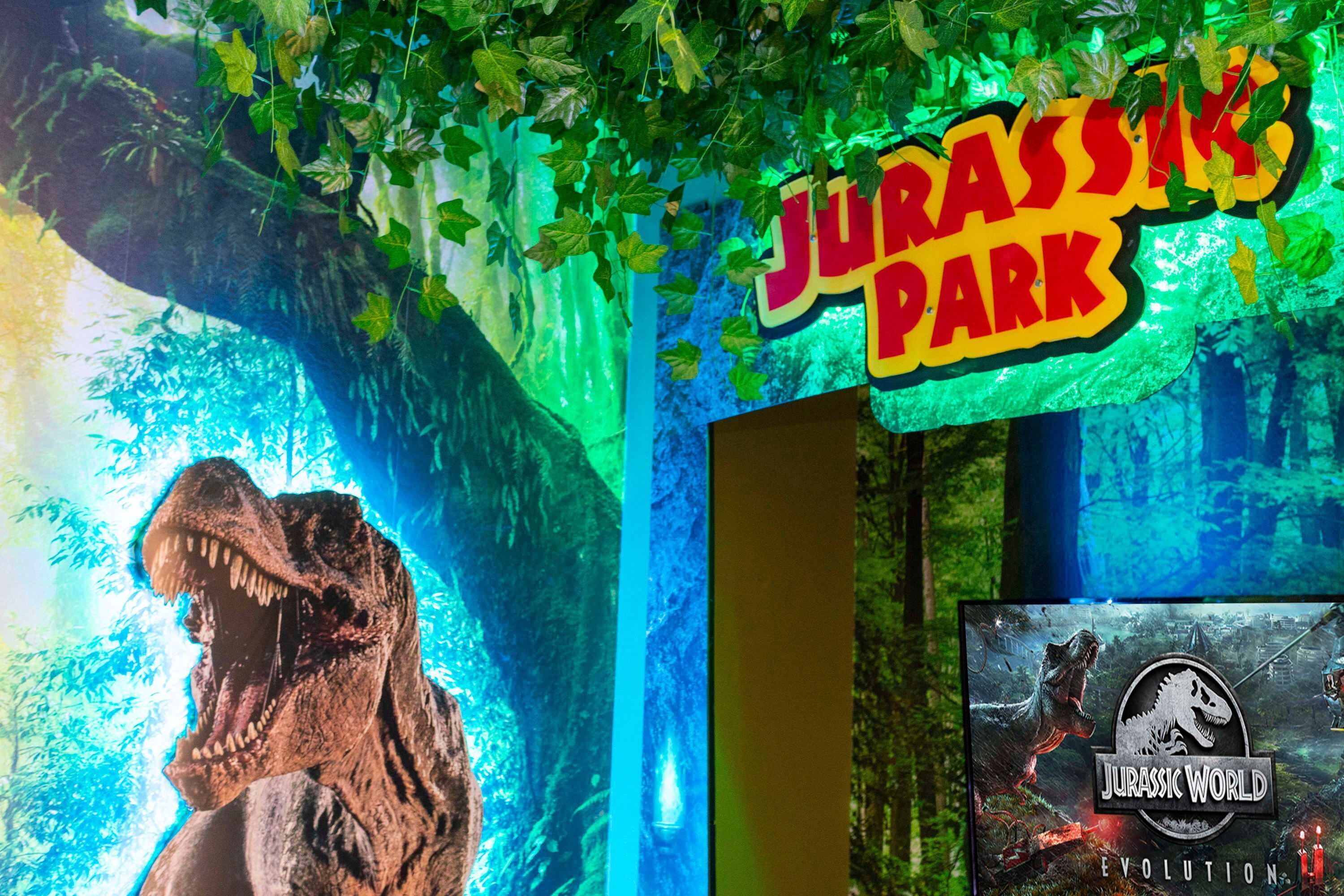 A dinosaur statue, a sign reading "Jurassic Park", and a movie poster for "Jurassic World: Evolution".