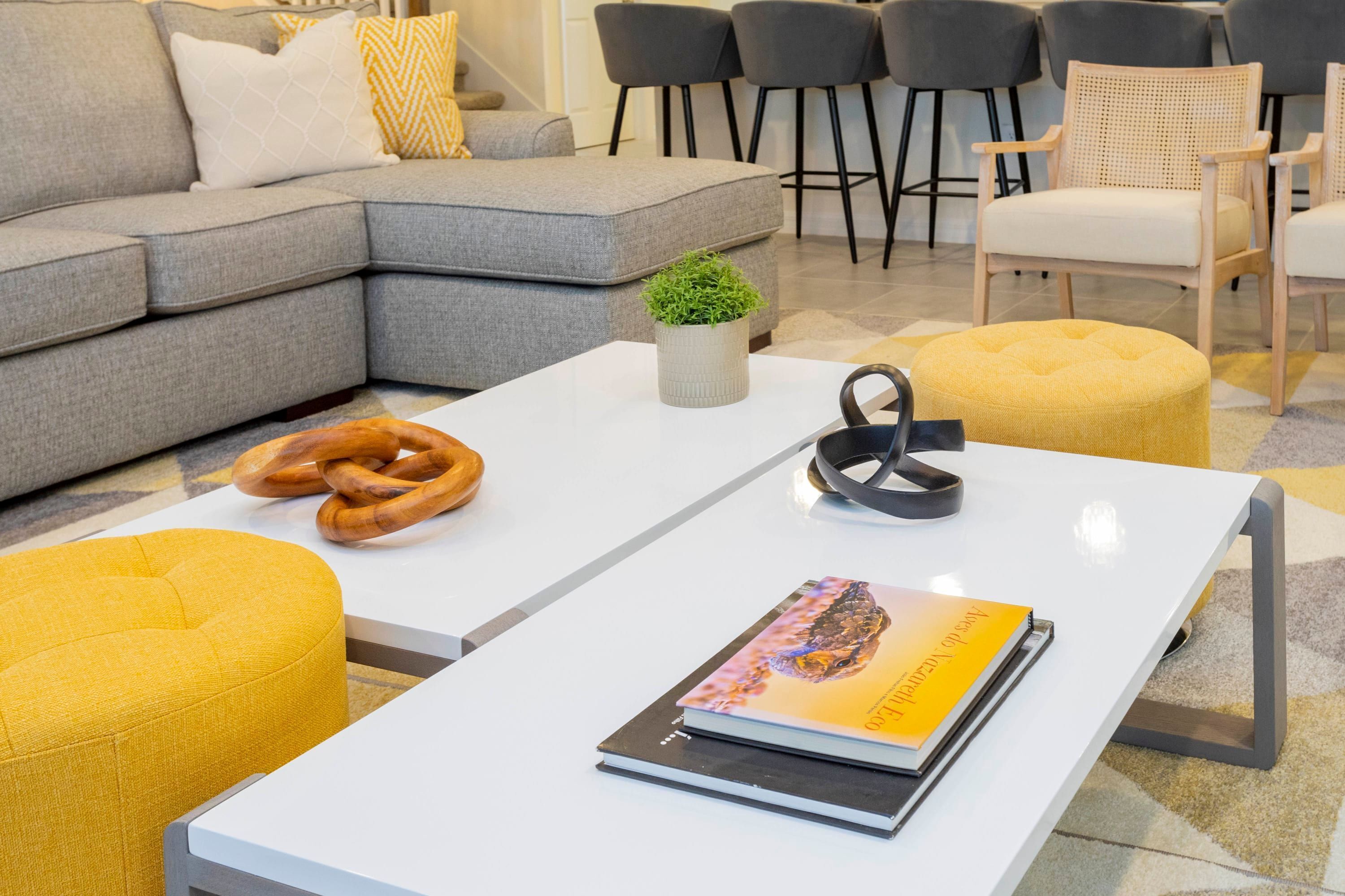 A modern living room with a grey sofa, yellow ottoman, white coffee table, and a book.