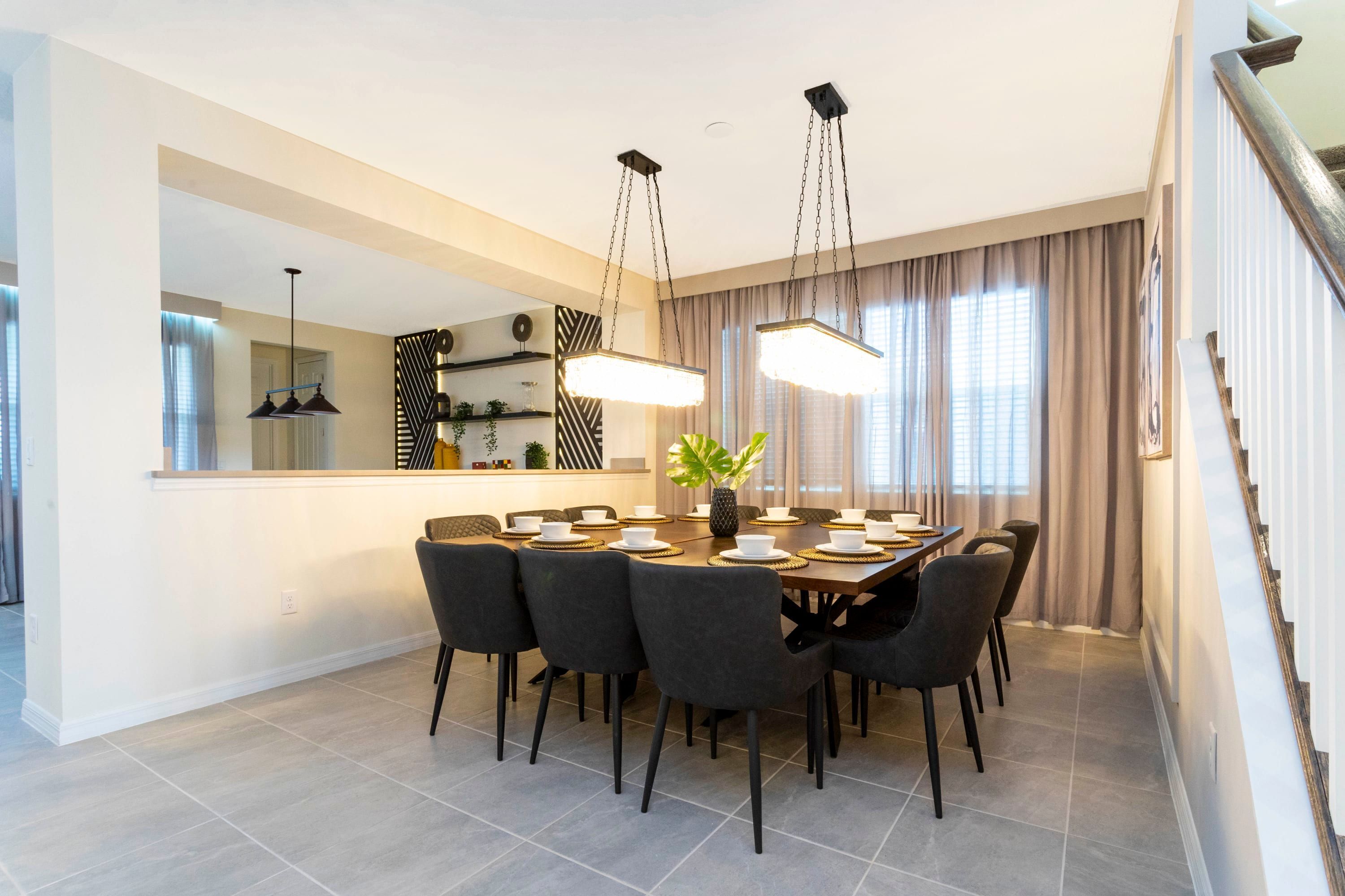 A modern dining area with a rectangular table set for six, surrounded by dark chairs. A large mirror and pendant lights hang above the table.
