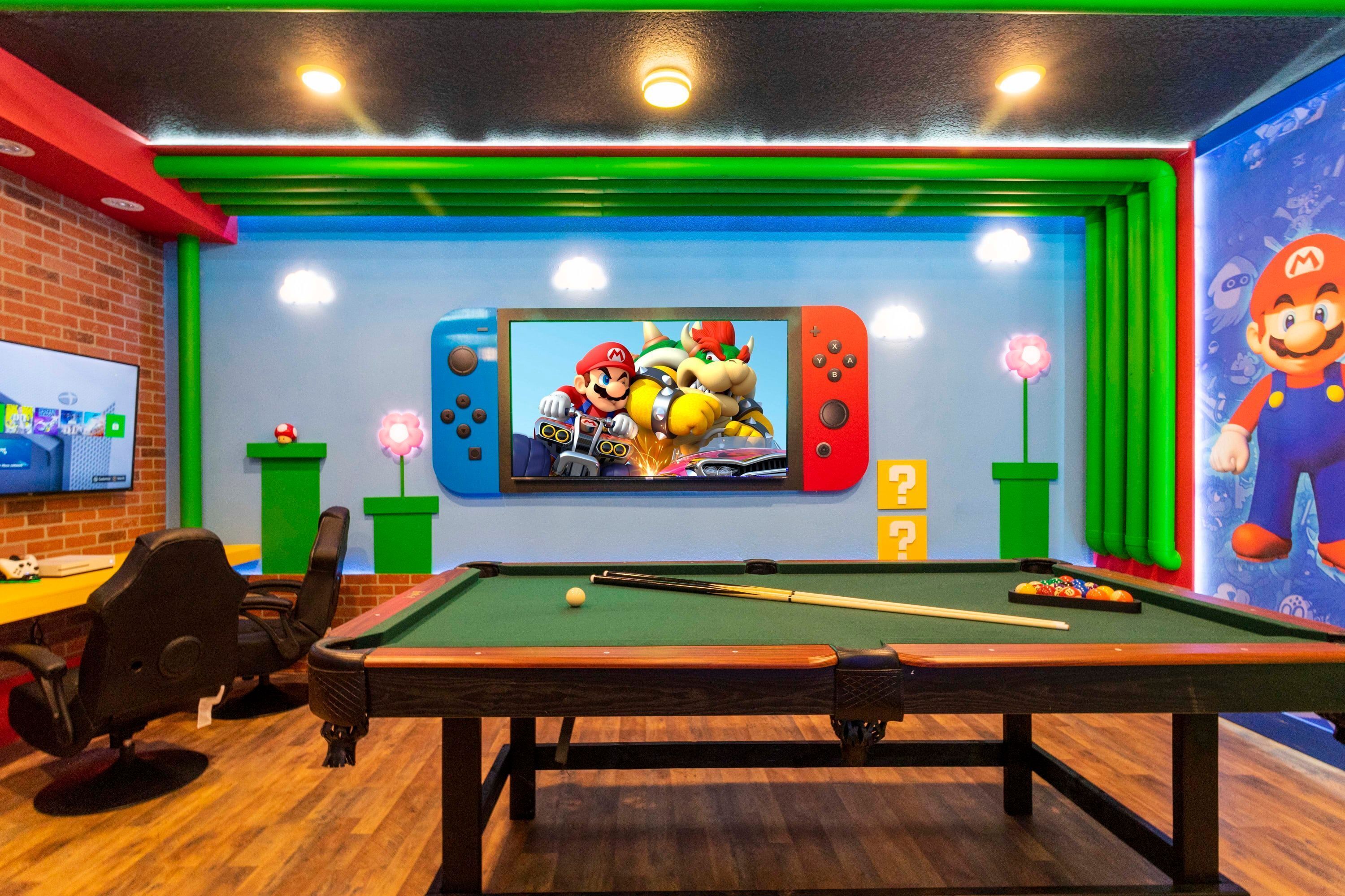 A pool table with a Nintendo Switch displaying a Mario game, surrounded by green and red decor, and a television on the left.