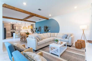 A modern living room with a large sofa, a coffee table, and a dining area with chairs and a table.