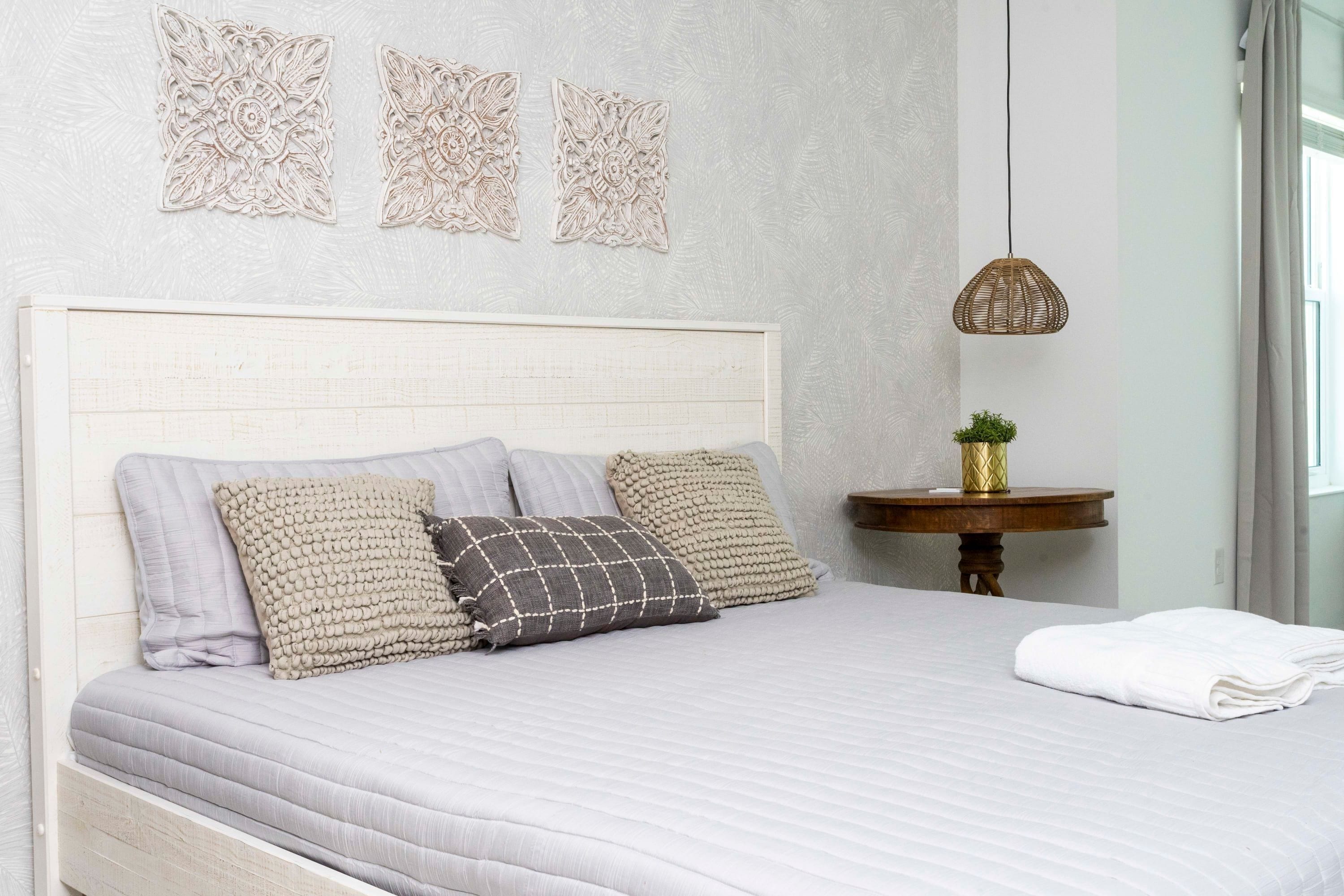 A neatly made bed with a white headboard, three pillows, and a white towel on the side.