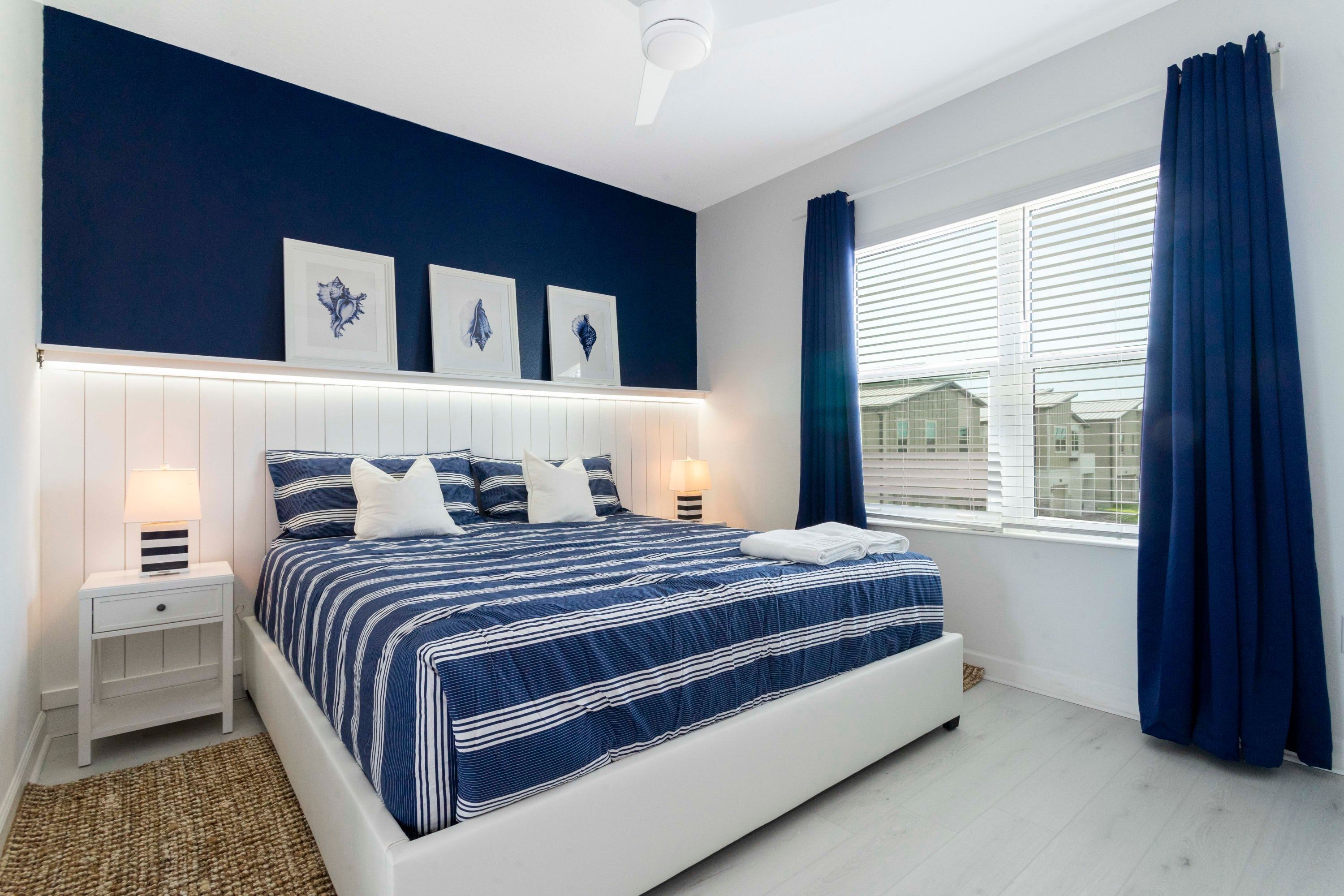 Un dormitorio con una cama grande, mesitas de noche blancas y una ventana con cortinas.
